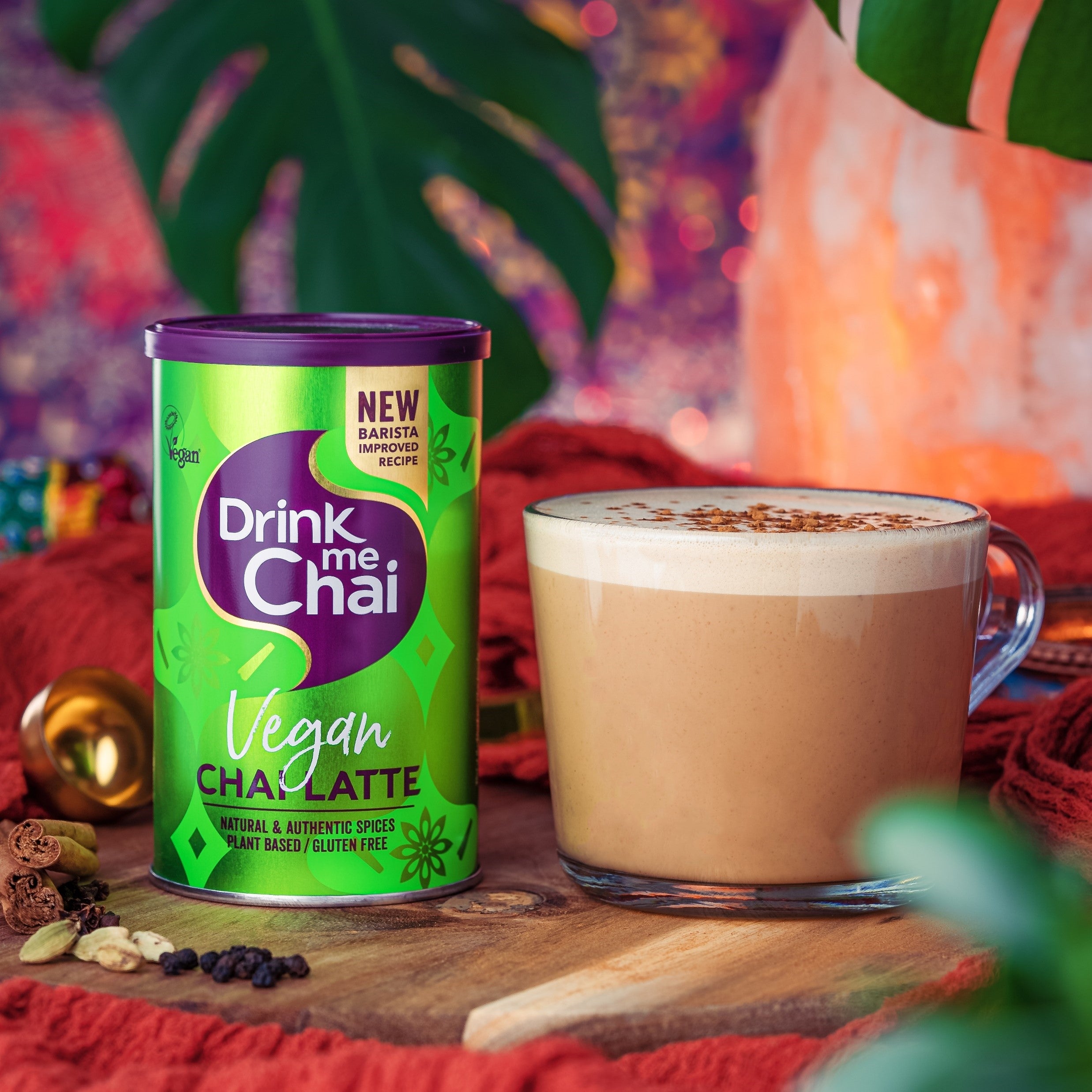 An alternative lifestyle image of a vegan chai latte tin of Drink Me Chai in the foreground with a latte glass filled with a chai latte slightly behind it
