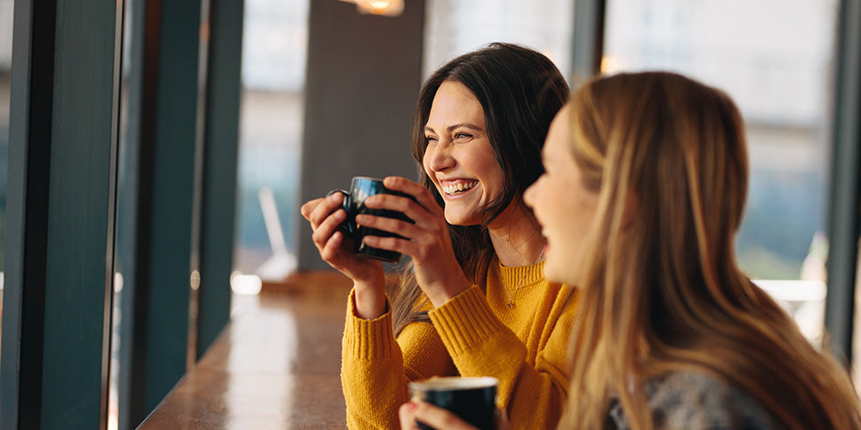 Two smiling ladies drinking cups of coffee in coffee shop 