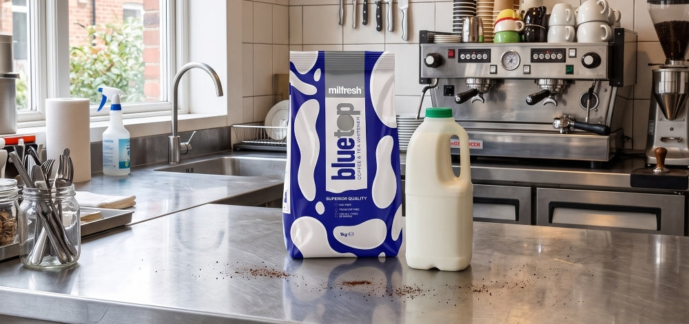 A 1kg pack of Milfresh Bluetop coffee whitener beside a bottle of fresh milk on a café worktop.