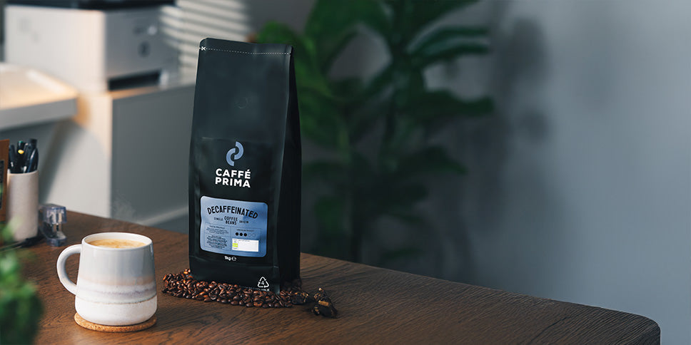 caffe prima decaf coffee beans pack on a kitchen table top nest to a cup of coffee