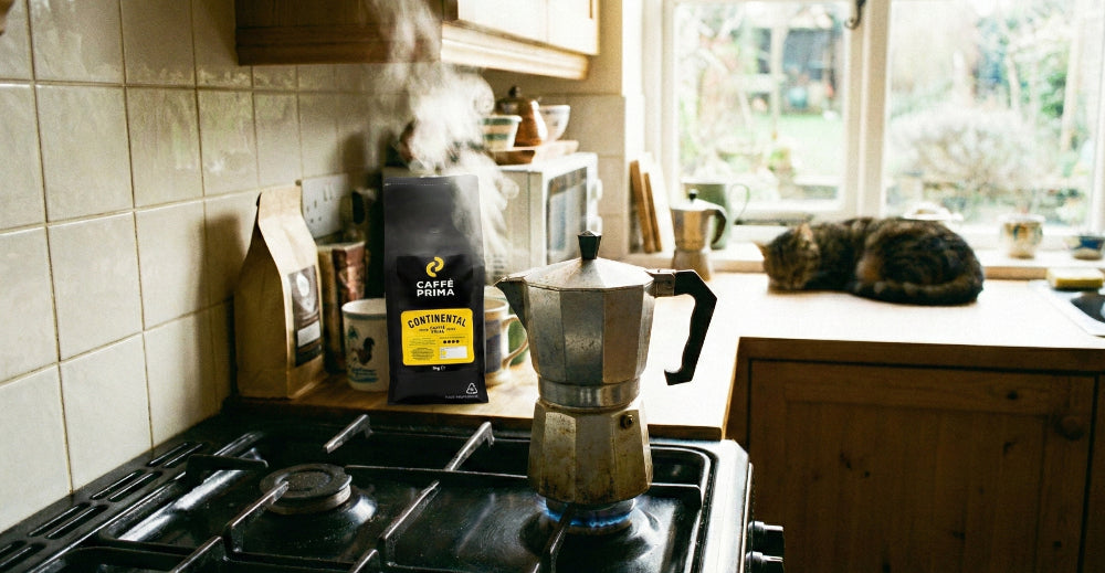 A bag of Caffe Prima coffee beans (Continental blend) next to a stove with a steaming moka pot